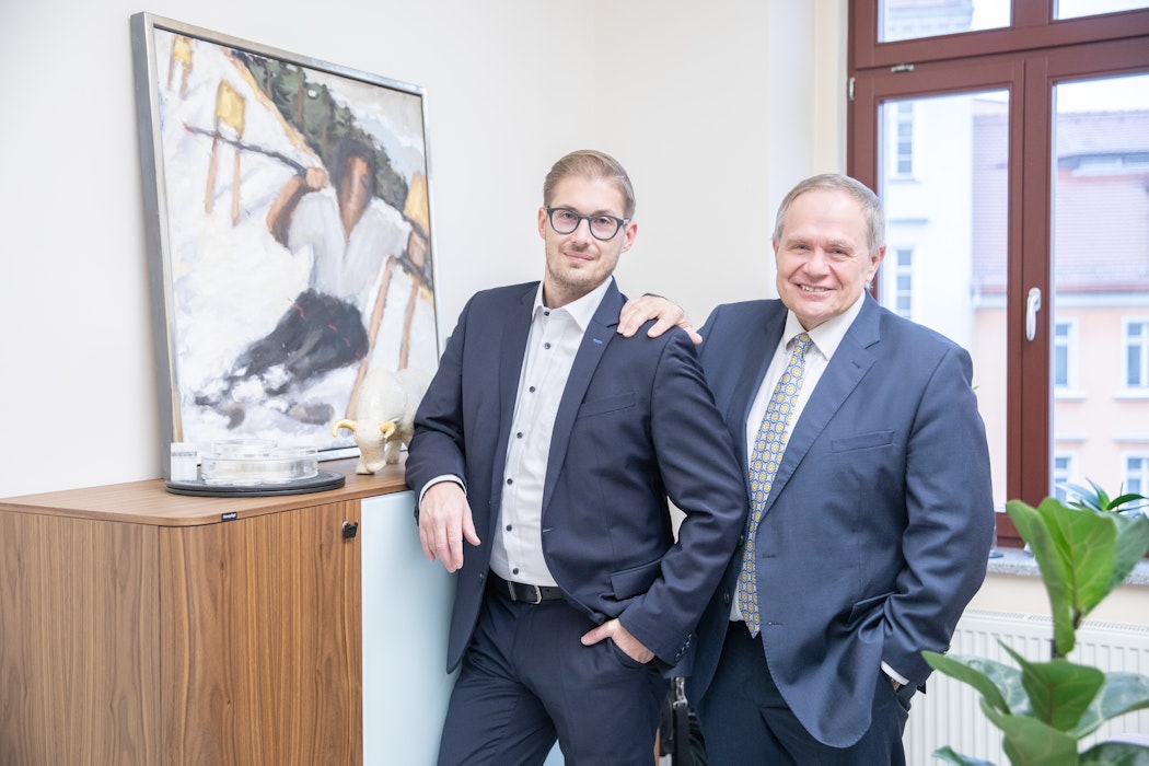 In einem hellen Raum hängt an der linken Wand ein Bild, daneben stehen die Gründer der Golden Gates AG Herbert Behr (Senior) und Constantin Behr (Junior).